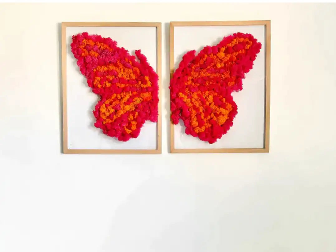Cuadros de mariposa naranja y rosada hechos de musgo de reno preservados colgados en la pared sobre una cama