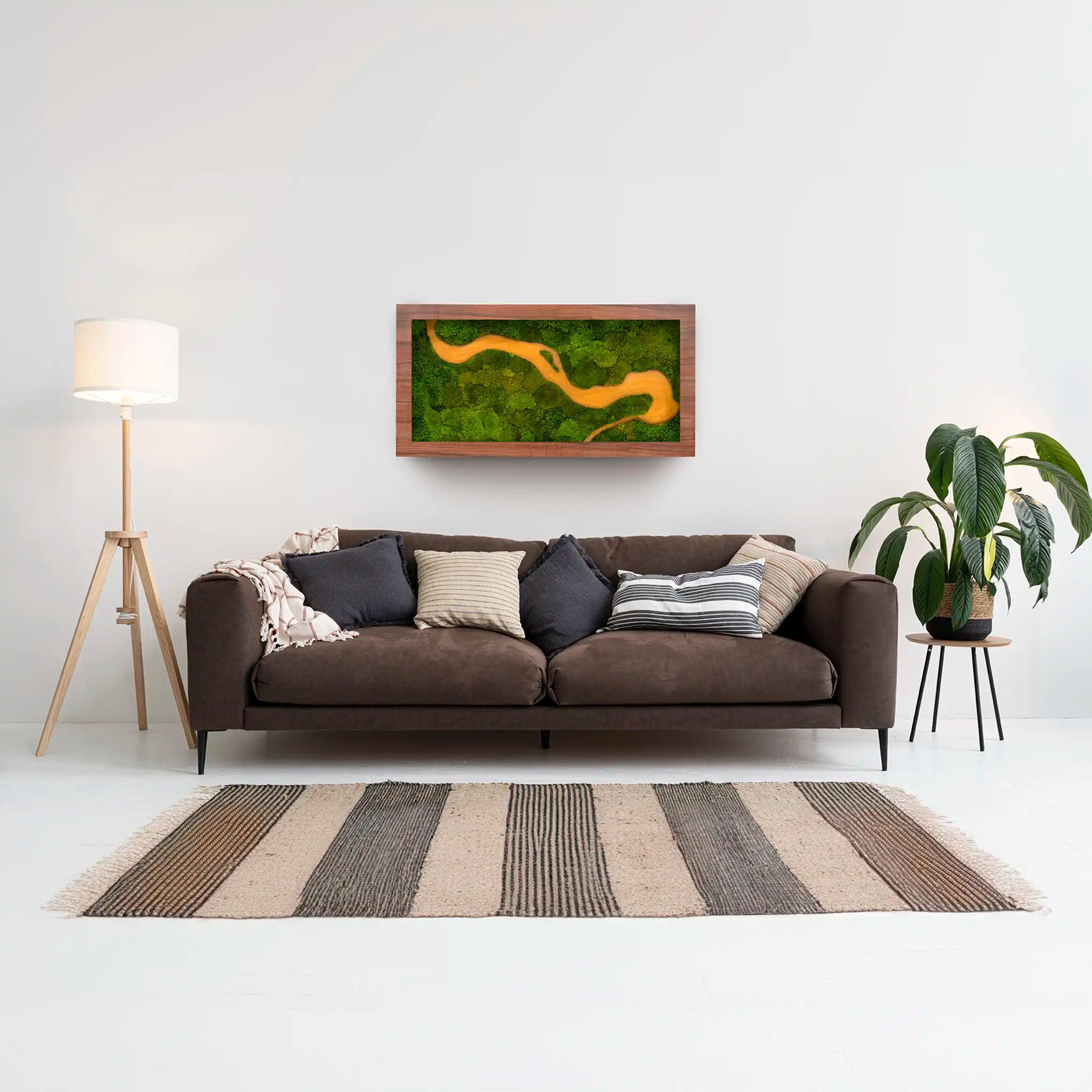 Sala de estar con sofá marrón y un cuadro decorativo de musgo preservado con figura de río amarillo en la pared.