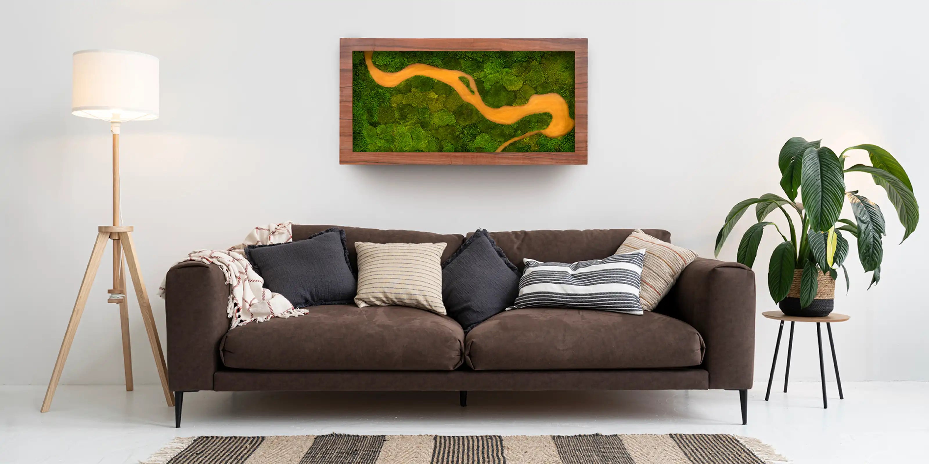 Sala de estar con sofá marrón y un cuadro decorativo de musgo preservado con figura de río amarillo en la pared.