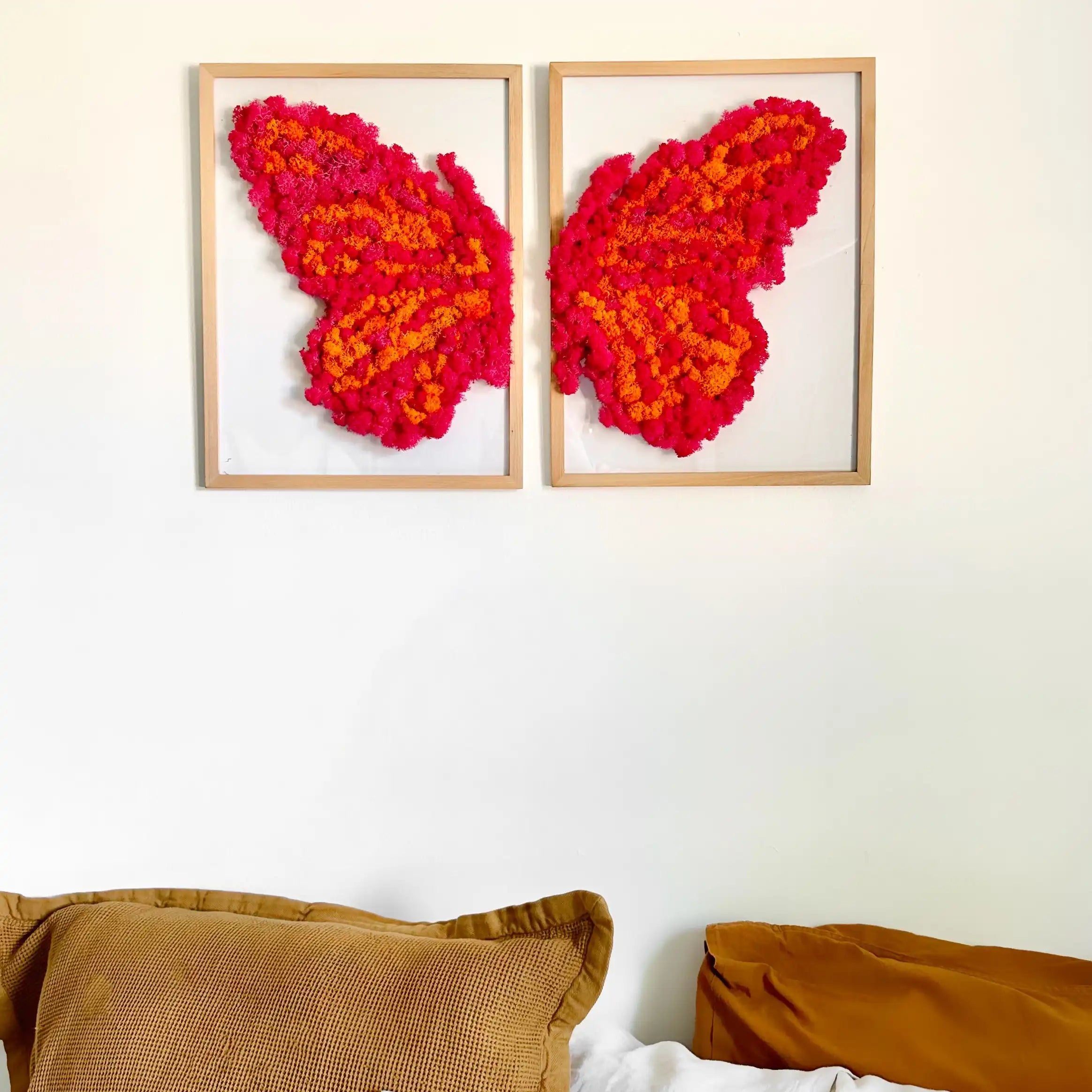 Cuadro decorativo de musgo preservado en forma de mariposa en la pared sobre una cama.