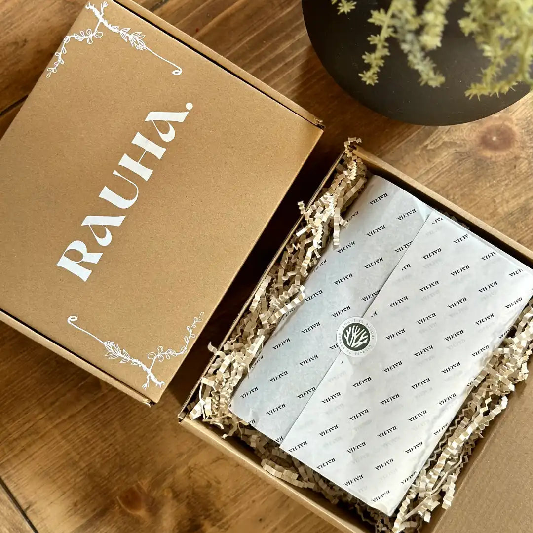Caja de embalaje de Rauha abierta mostrando el contenido con papel de seda y relleno decorativo.